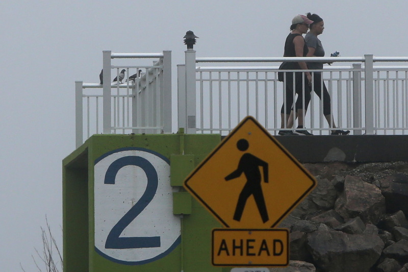 Two signs combined rightfully point out that two pedestrians are walking atop the Harborview Walk in the sound end of New Bedford.  The large two signifies that this is the second storm barrier door which can be closed if a hurricane or storm were to strike the region.  PHOTO PETER PEREIRA