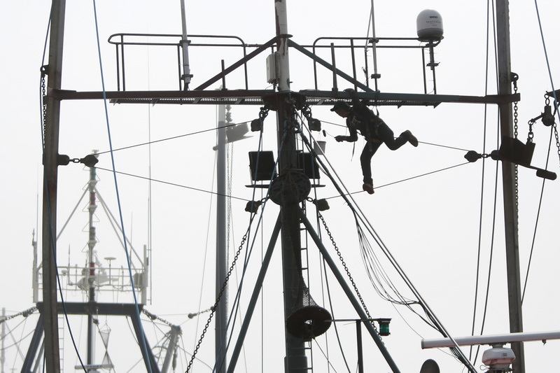 A painter walks the high wire, as he paints the mast of a fishing boat in New Bedford, MA.  PHOTO PETER PEREIRA