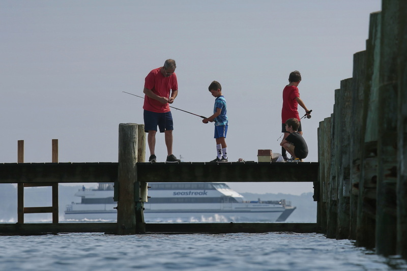 (top) A man helps some youngsters with the bait on their line, as they enjoy a morning of fishing from a pier in the south end of New Bedford.  In the distance the Seastreak high speed ferry can be seen making its way to Martha's Vineyard. (below) Young and old alike, take shelter from the heat by jumping off of the Little River Road bridge in Dartmouth, MA.  PHOTOS PETER PEREIRA