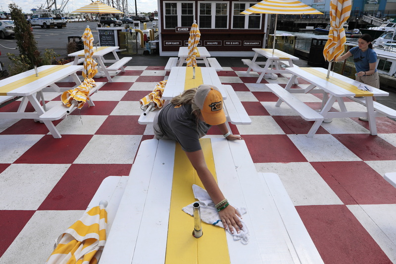 Marcie Araujo, center, and Abby Lopes, right, clean the Clam Bar tables set on a colorful ground, before opening time on New Bedford's waterfront. PHOTO PETER PEREIRA