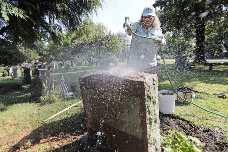 Deborah Thompson of Loving Touch Grave Site Care, sprays the headstone with water, before scrubbing it and landscapes the area around it at Riverside Cemetery in Fairhaven, MA.  PHOTO PETER PEREIRA