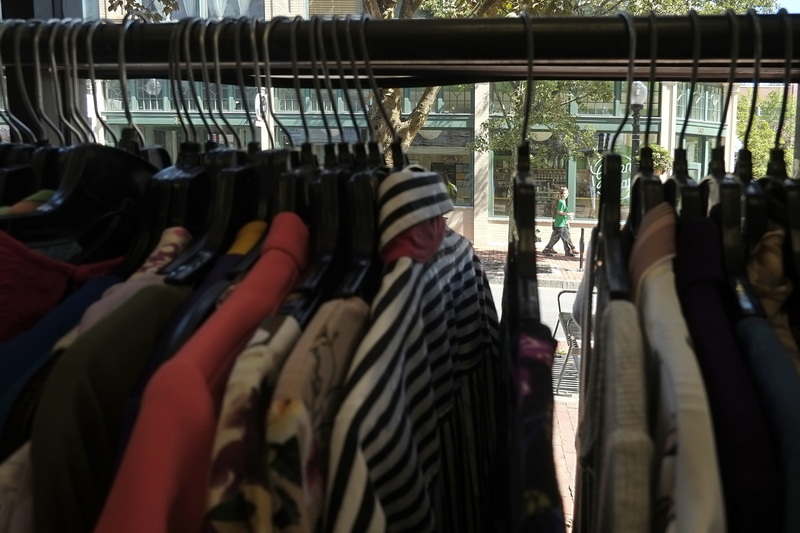 A woman is seen walking up Purchase Street in New Bedford, as seen through a gap in the hangers of women's clothing for sale inside The MadLila clothing store in downtown New Bedford, MA.  PHOTO PETER PEREIRA