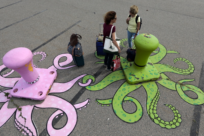 Two women who had just arrived on the ferry from Nantucket, are entraped by the octopi painted bollards, as they wait for their ride to arrive at State Pier in New Bedford, MA.