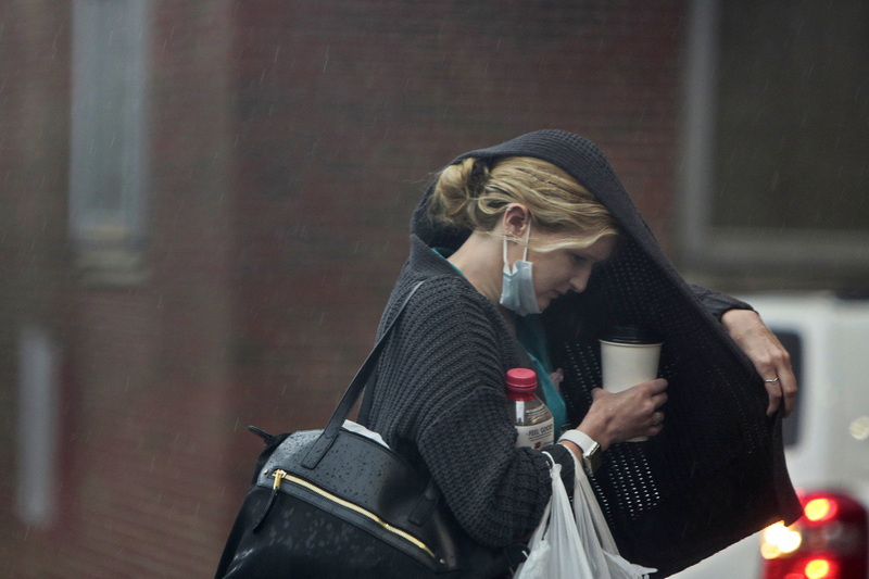 A woman tries o shield her head and her coffee with her sweater, from the driving rain in downtown New Bedford, MA.  PHOTO PETER PEREIRA