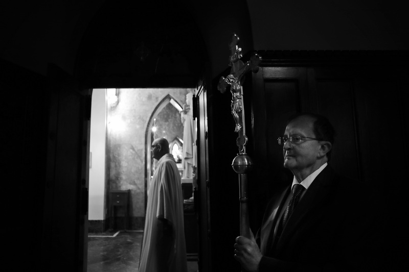 Eucharistic minister, Donal Buckley, holds a crucifix as Father Michael Racine, is seen looking to see if everything is in place before conducting a funeral mass at St Lawrence Martyr Church on County Street in New Bedford which is celebrating its 200th anniversary, PHOTO PETER PEREIRA