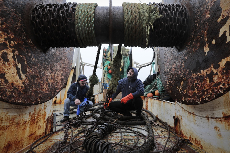 Edward Combs, left, joins Captain Antonio Cravo in preparing the gear for a new net they will install on the huge drum in front of them aboard the fishing boat United States docked in New Bedford, MA.  PHOTO PETER PEREIRA