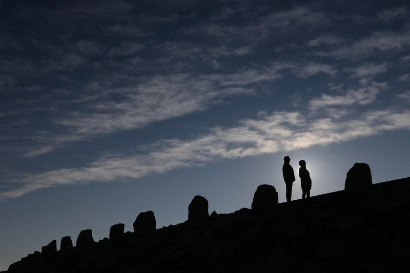 The sun rises behind two women looking out into Buzzards Bay from the top of the Hurricane Barrier at Fort Phoenix in Fairhaven, MA. 