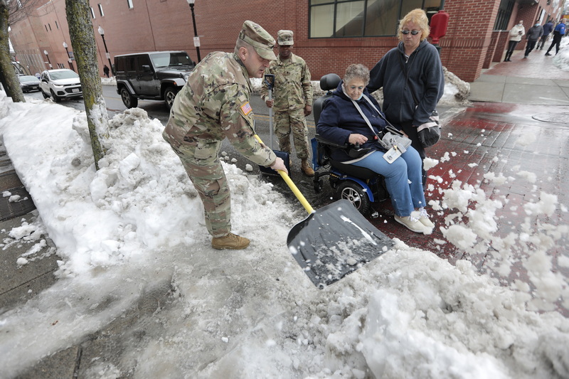 Army National Guardsmen SSG Nathan Castonguay and SPC Everald Hermitt clear the entrance to the sidewalk in front of their just opened recruitment office on Elm Street in New Bedford, MA when they noticed Marjorie Oliver trying to get on the sidewalk using a motorized wheelchair.