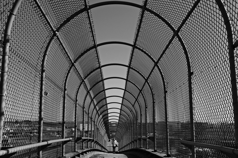 A woman is surrounded by a cathedral of steel, as she makes her way across the Route 18 pedestrian bridge in New Bedford, MA. PHOTO PETER PEREIRA