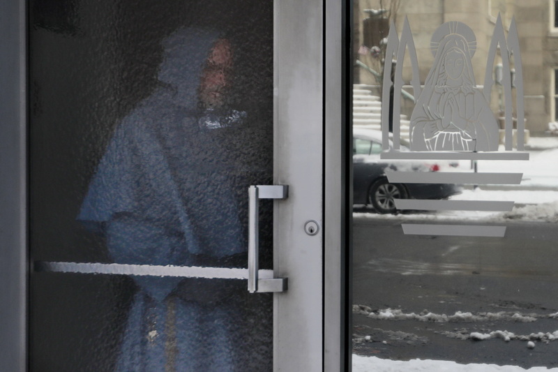 Franciscan Friar, Father Allen, stands behind the textured glass door to Our Lady's Chapel in downtown New Bedford, MA in an effort to stay warm as he waits for his ride to arrive. PHOTO PETER PEREIRA