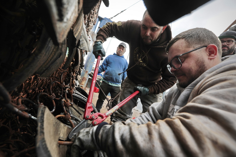 (l to r) Luis Linares, Fernando Gonsalo, Giovanni Pinto (mate) and Bobby Amaral of the fishing boat George's Banks, install sections of used tires to the bottom of a scallop dredge to protect it when it scrapes across the seafloor, before heading back out to sea from New Bedford, MA. PHOTO PETER PEREIRA