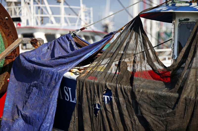 A painter is seen through the temporary dust barriers as he scrapes the paint of the Tom Slaughter II fishing boat in New Bedford, MA before giving the dragger a new coat of paint. PHOTO PETER PEREIRA