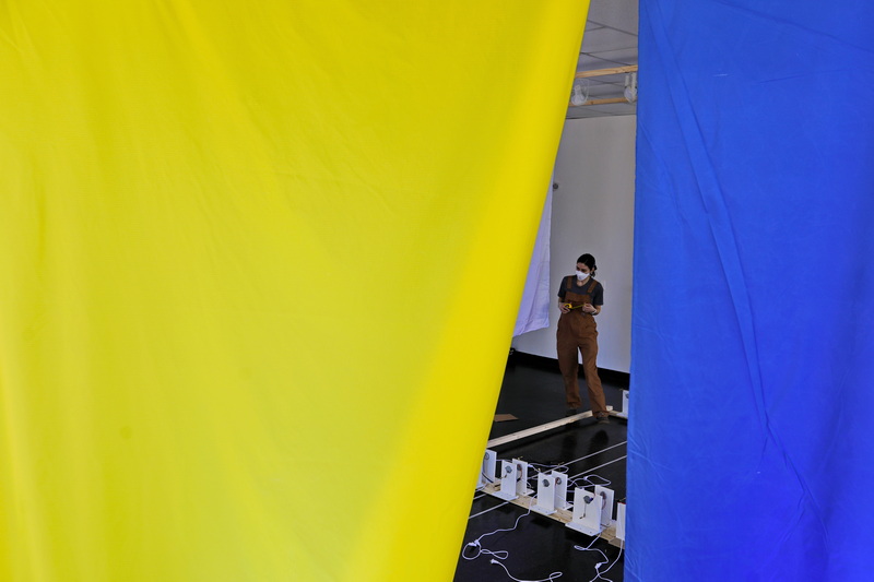 UMass Dartmouth student Katie Rodden Walker prepares her art installation to be shown in the UMass Dartmouth Star Store gallery, as seen through an Ukrainian flag installed by the staff in solidarity with the Ukrainian people. PHOTO PETER PEREIRA