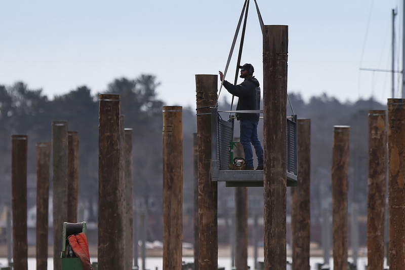 A worker finds himself suspended by a crane as he installs new piles on the Wareham River in Wareham, MA. PHOTO PETER PEREIRA