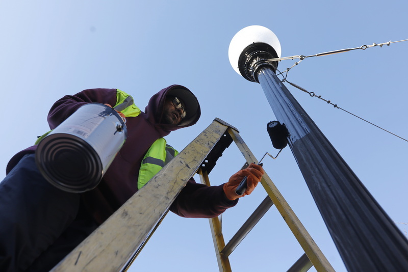 Nick Ribeiro puts a fresh coat of paint on a light post at Custom House Square in downtown New Bedford, MA.  PHOTO PETER PEREIRA