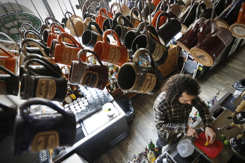 A J Monteiro, bartender, prepares the bar  of the Pour Farm Tavern for opening on Purchase Street in downtown New Bedford, MA.  Above him the hundreds of beer mugs for those participate in the Mug Club. PHOTO PETER PEREIRA