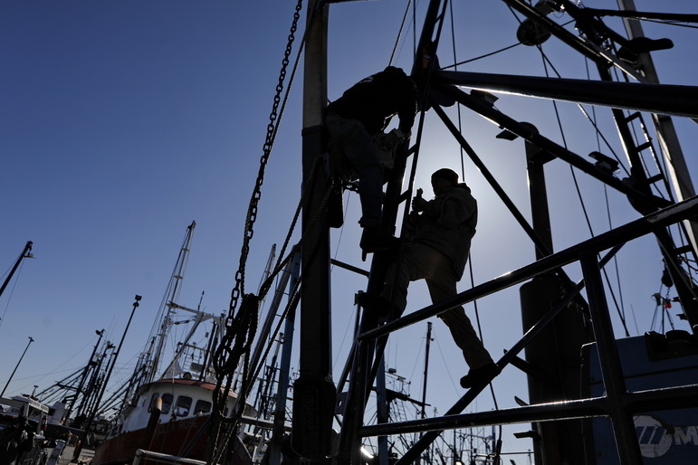 Fishermen are seen up high , making repairs to the masts of a fishing boat docked in New Bedford, MA.  PHOTO PETER PEREIRA