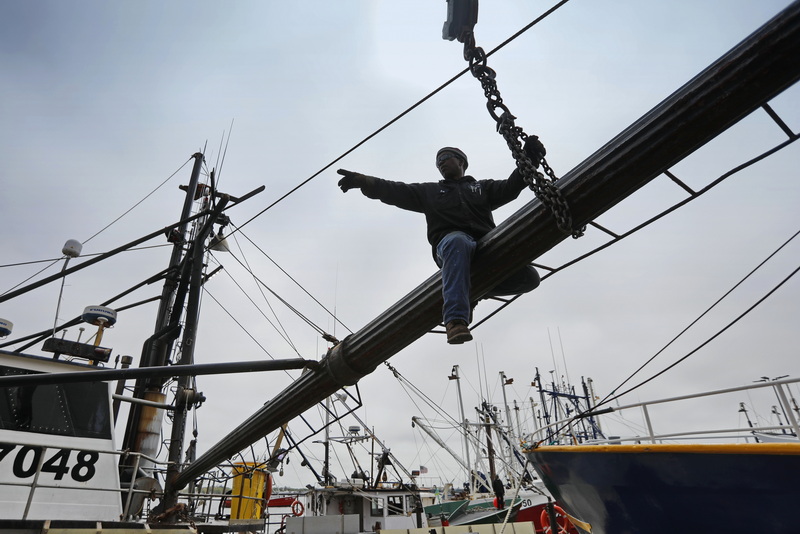 Blue Fleet welder, Sal Sequeira, directs proceedings from above as he is seen straddling an outrigger he repaired on a fishing boat in New Bedford, MA. PHOTO PETER PEREIRA