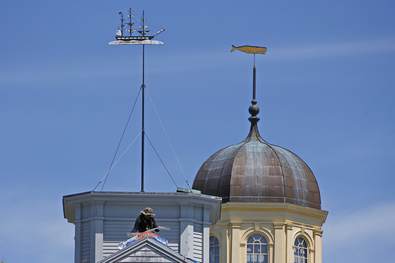 A roofer replaces the shingles on the roof of the Seamen's Bethel as in the background the weathervanes re-enact history, with the ship atop the Seamen's Bethel chasing the whale atop the Whaling Museum in the distance. PHOTO PETER PEREIRA