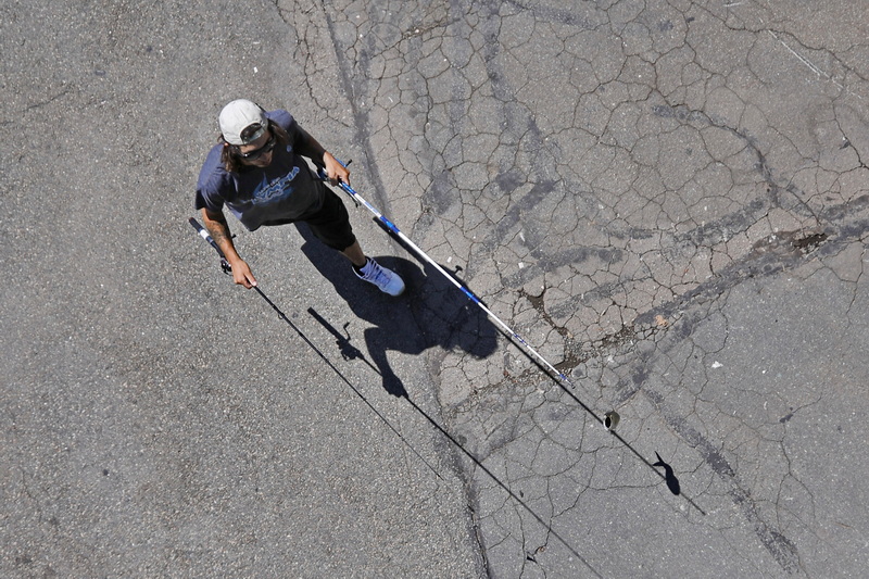 The shadow of the fish a man caught can be seen on the ground, as he makes his way under the Fairhaven bridge in New Bedford, MA with two fishing rods in hand.  PHOTO PETER PEREIRA