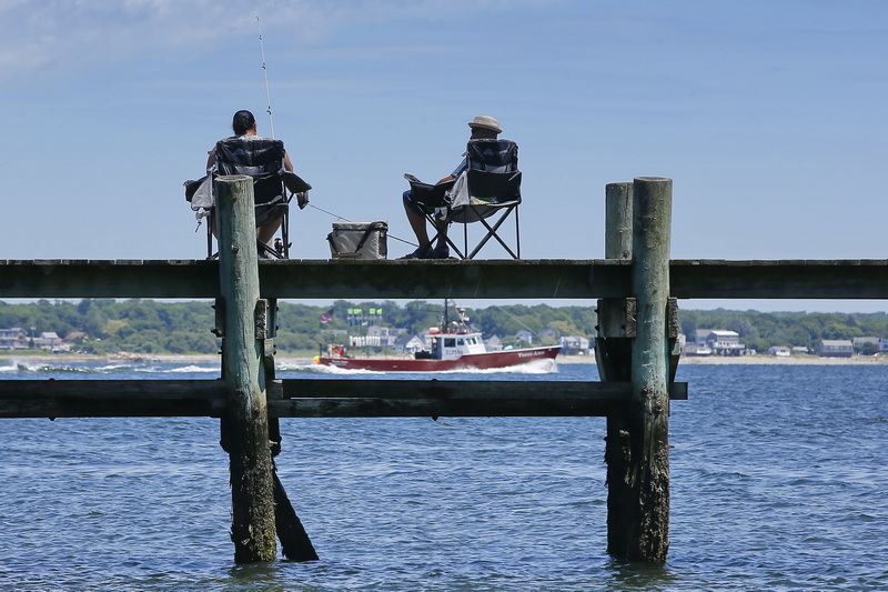 A man and woman enjoy a morning of fishing on a dock in the south end of New Bedford, MA as a boat heads out to sea.  PHOTO PETER PEREIRA