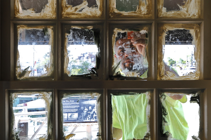 Jose Ramos uses a razor blade to scrape the excess paint from the freshly painted muntins on the windows of the soon to open Marisol's Express on New Bedford's waterfront.  PHOTO PETER PEREIRA