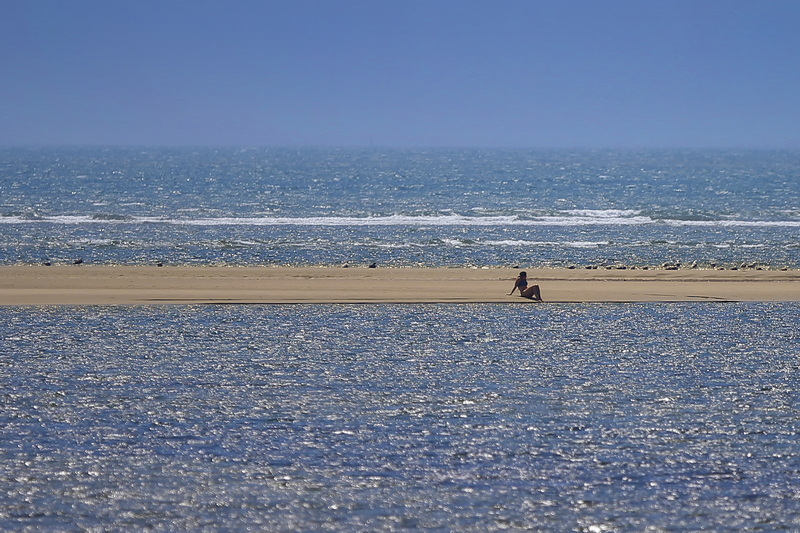 A woman sits between the Atlantic Ocean, background, and the Slocum River, foreground, on a sandbar which appears at low tide off Little River Road in Dartmouth, MA.  PHOTO PETER PEREIRA