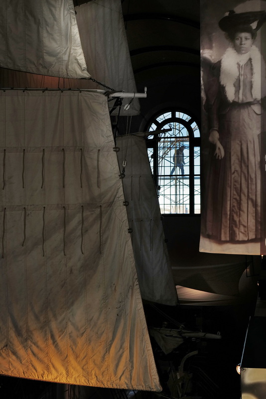 A mason walks across the large window of the Whaling Museum's Lagoda room in New Bedford, MA. The sails of the 1/2 scale whaleship Lagoda are seen on the left while on the right a poster celebrating Cape Verdean culture. PHOTO PETER PEREIRA