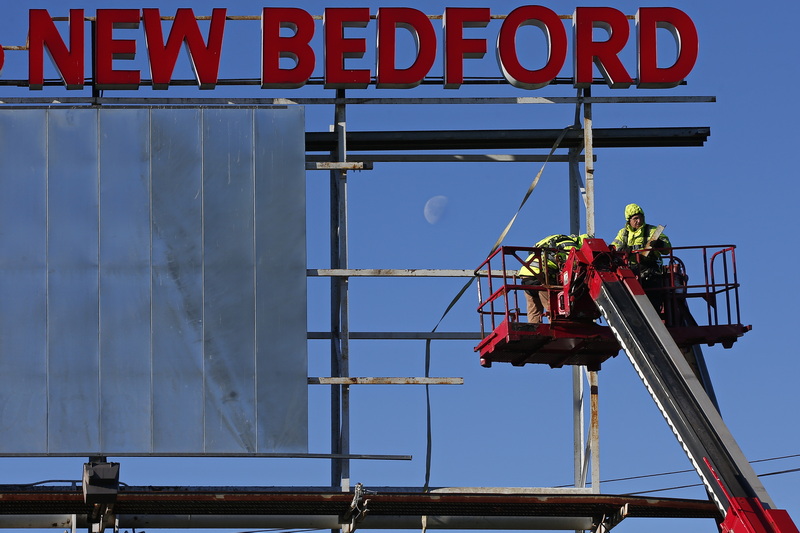 Two workers from Poyant Sign make repairs to the billboard welcoming visitors to New Bedford on the edge of Route 195, while the moon can be seen between the framework of the panel they are repairing.  PHOTO PETER PEREIRA