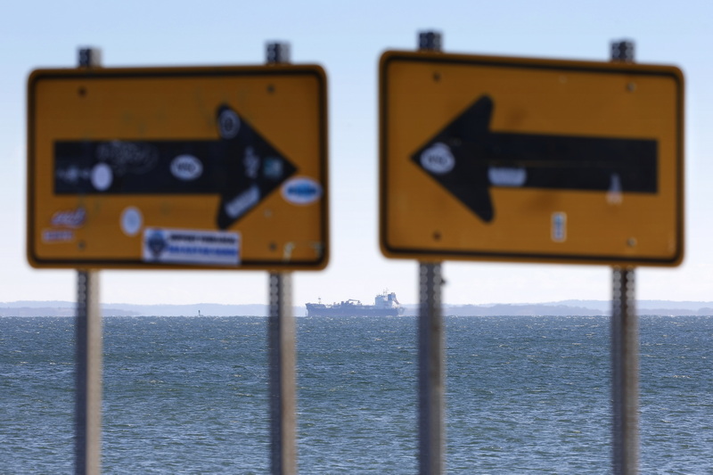 A large tanker ship is seen crossing Buzzards Bay in the distance, between two traffic signs pointing at each other on East Beach in Westport, MA.  PHOTO PETER PEREIRA