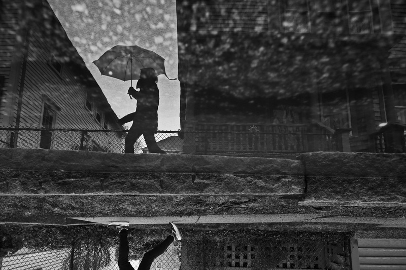 A woman is reflected on a puddle on the side of the road as she makes her way up Union Street in New Bedford, MA on a rainy day.. PHOTO PETER PEREIRA