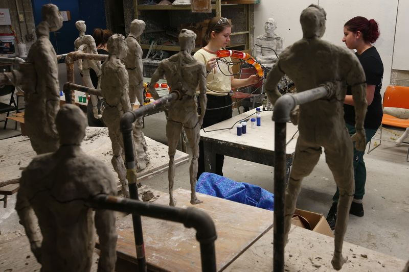 Clay-on-wire figures from body as concept class look on, as Katie Erwin and Maddie Gonzalez work on the head of the nips bottles monster.  The 'Monster Creature from the Plasticine Era' made with over thirty two thousand discarded nips bottles around a metal framework, will be marched by students in the upcoming A-Ha Earth Eve Procession in downtown New Bedford. PHOTO PETER PEREIRA