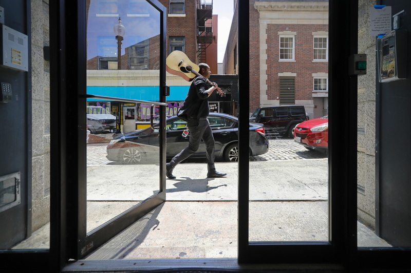 Hugo Amarante walks up William Street with a guitar on his shoulder past the open door of an apartment complex.  When asked where he played his guitar, he responded 