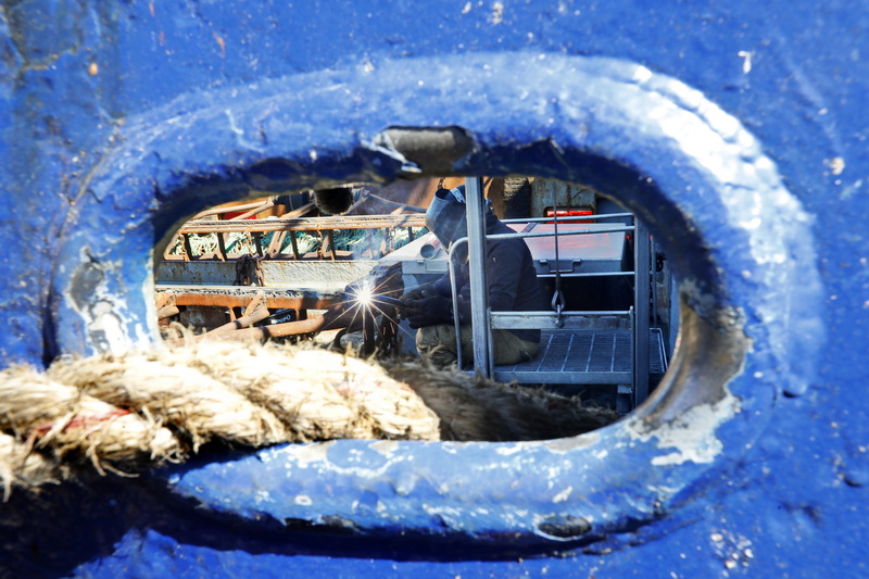 Jose Lopez welds new end plates to the dredges of the scalloper Guidance as seen through an haweshole of the fishing boat docked in New Bedford, MA PHOTO PETER PEREIRA