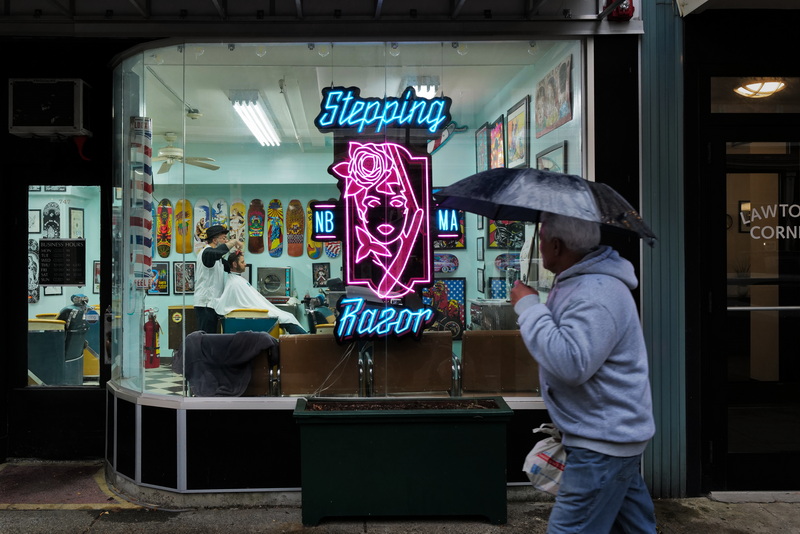 Danny Baptista, owner, gives Alex Buchanan a haircut inside of the Stepping Razor barber shop on Purchase Street in New Bedford, MA as a man takes shelter from the driving rain with an umbrella as he walks past outside. PHOTO PETER PEREIRA