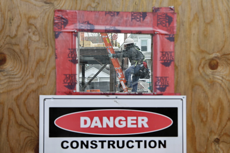 A worker makes his way up a ladder as seen through the small window glued to the entrance door to the construction site of an apartment building being constructed at the former RMV building on Union Street in New Bedford, MA.  PHOTO PETER PEREIRA