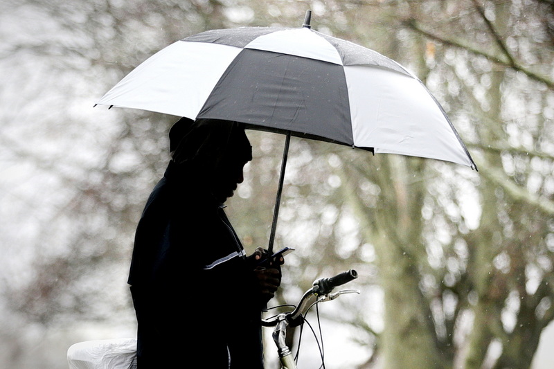 A man browses his phone under an umbrella as he waits for the crossing light on Pleasant Street in New Bedford, MA on a riany morning.  PHOTO PETER PEREIRA