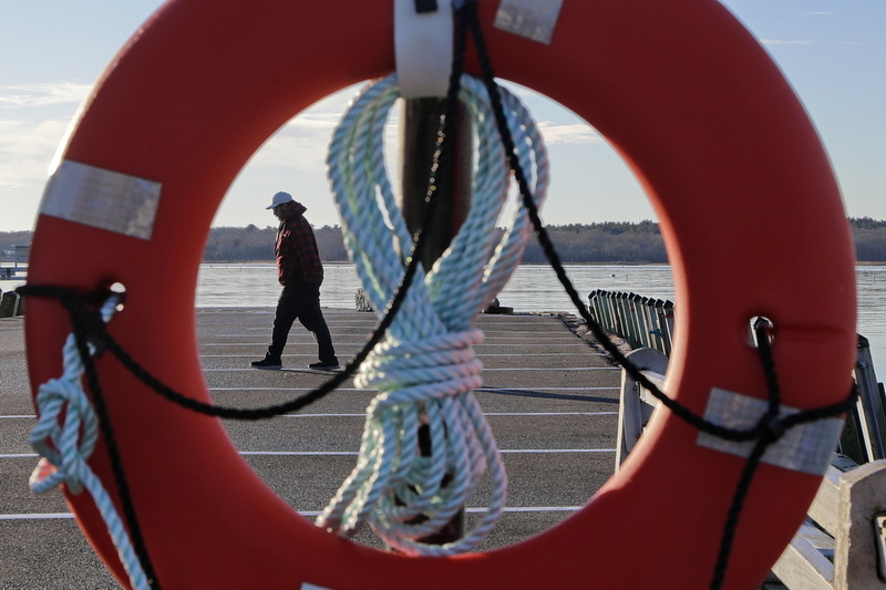 Mike Behan goes for a morning walk on the wharf in Mattapoisett, MA as seen through a life ring buoy hanging on the side in case of emergency.  PHOTO PETER PEREIRA