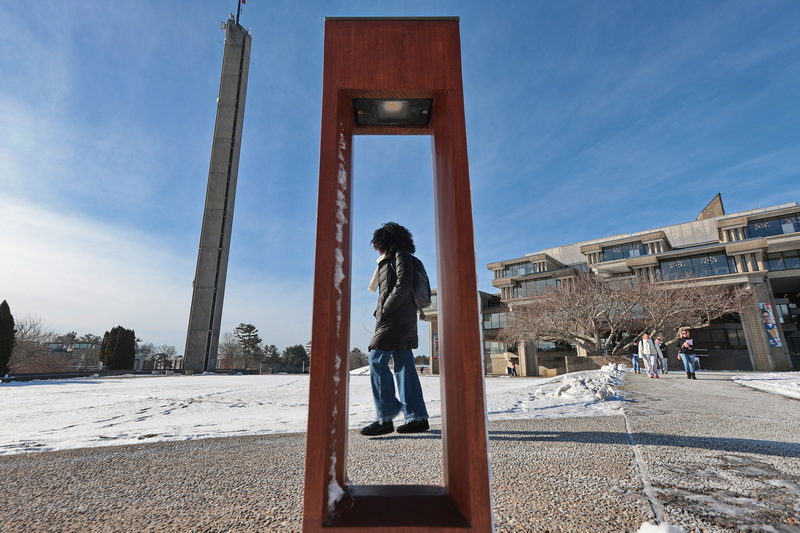 A woman makes her way across the UMass Dartmouth campus, as seen through a light fixture which reflects the campus' brutalist architecture, as temperatures continue in the single digits across the region. PHOTO PETER PEREIRA