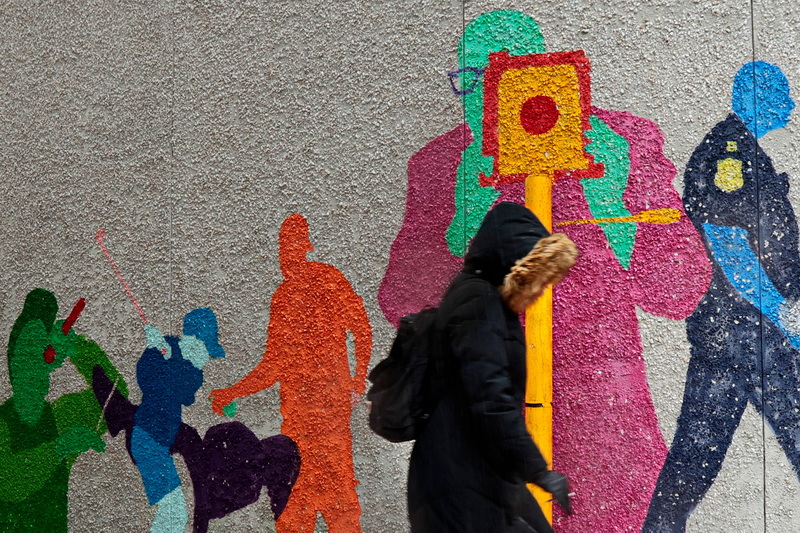 A woman has her photo taken by one of the painted figures on the walls of Sears Court in downtown New Bedford, MA on a cold snowy day. PHOTO PETER PEREIRA