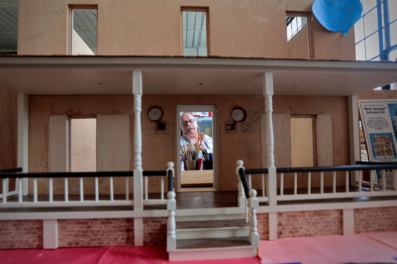 Bob Sequer works on a dollhouse as seen through the front door of another project he still needs to finish at Flip this Dollhouse at the Killburn Mill in New Bedford, MA. PHOTO PETER PEREIRA