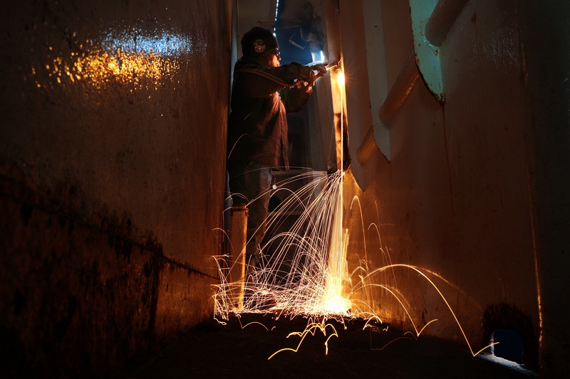 Sal Sequeira, a welder from Blue Fleet, sends sparks flying while cutting a metal panel from the hull of a fishing boat that is docked in New Bedford, MA while working from the inside. PHOTO PETER PEREIRA