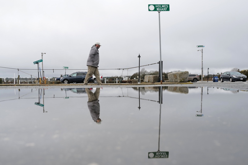 A man is reflected in a large puddle of water as he makes his way across Holmes Wharf in Mattapoisett, MA on a rainy morning. PHOTO PETER PEREIRA