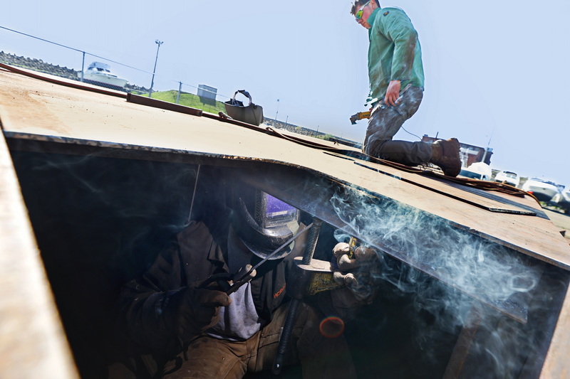 Miles Ostiguy grinds the gaps between the plates above, as Dan Sutterfield welds them below in the barge they are making at Fitzerald Metal Works in New Bedford, MA. PHOTO PETER PEREIRA