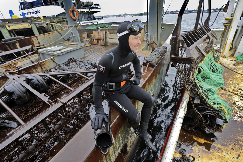 James Mercer takes a break between dives on a cold rainy day, as he untangles ropes from the propeller of a fishing boat docked on State Pier in New Bedford, MA. PHOTO PETER PEREIRA