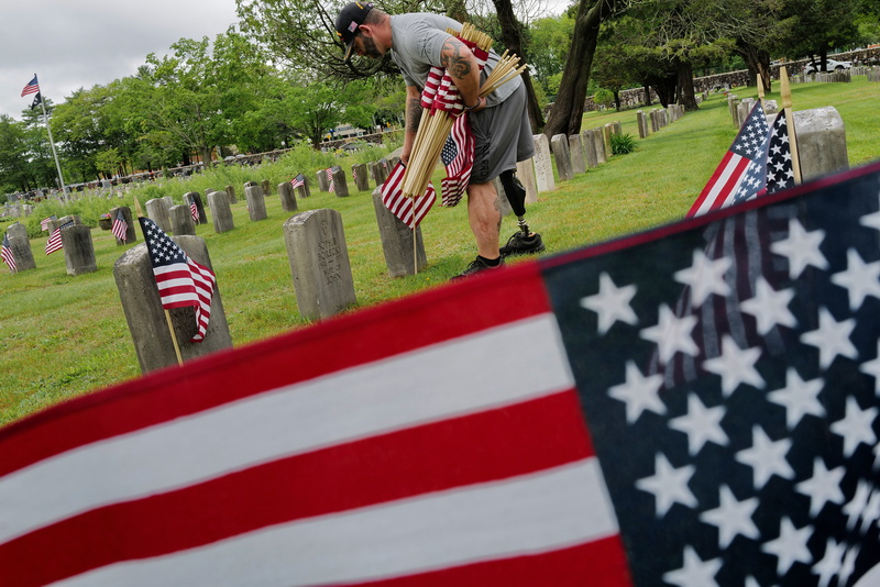 Christopher Gomes, veteran agent for the city of New Bedford, sets American flags at the graves of veterans interred at Pine Grove Cemetery in anticipation of Memorial Day. Mr. Gomes, a veteran of the Army, lost his right leg due to an IED explosion while he was serving in Iraq in 2008. PHOTO PETER PEREIRA