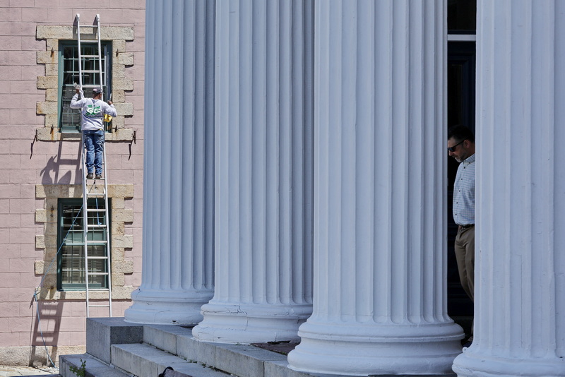 A painter applies paint to the window frames of the Candela Cucina building while a man exits the J.J. Best Banc & Co building, passing by its famous colonnade on N Front Street in downtown New Bedford, MA PHOTO PETER PEREIRA