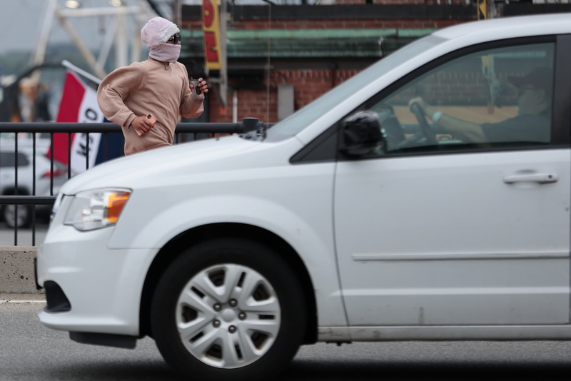 A motorist driving up Route 18 looks over at a woman jogging southward on the sidewalk in New Bedford, MA. PHOTO PETER PEREIRA