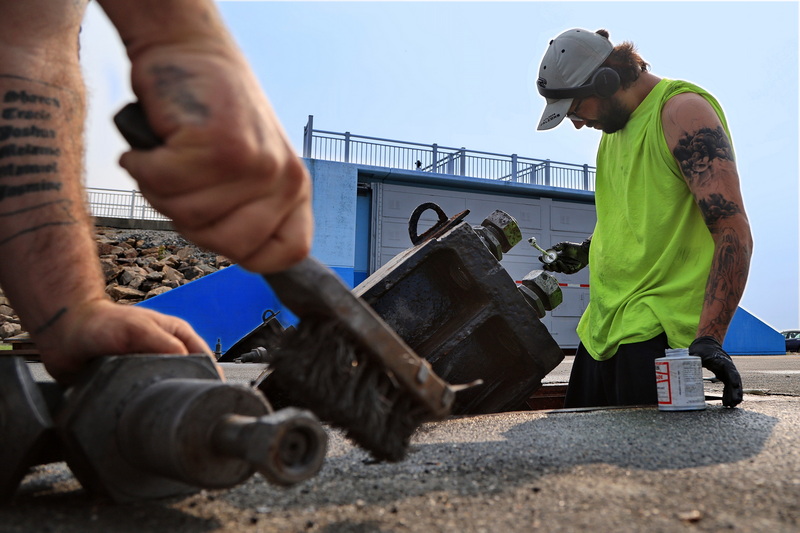 Tyler Washburn uses a wire brush to eliminate rust, while Rob Costa applies anti-seize grease to the connectors that are utilized to secure the hurricane barriers in storm conditions in New Bedford, MA as part of maintenance work in readiness for hurricane season. PHOTO PETER PEREIRA