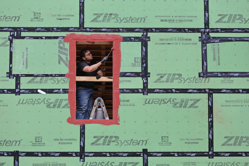 A carpenter is framed by his work as he applies moisture protection paint around the window frame of a house being constructed in Dartmouth, MA. PHOTO PETER PEREIRA
